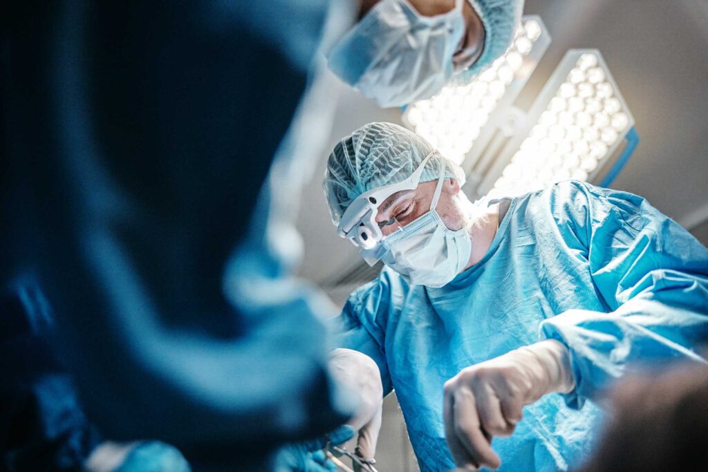 Chirurgo concentrato durante un intervento in sala operatoria, indossa camice sterile, mascherina e lenti ingrandenti, con luci chirurgiche sullo sfondo
